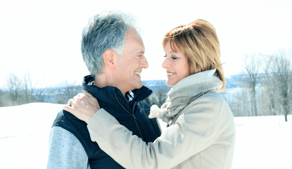 Ein älteres Paar steht im Schnee und lächelt sich an