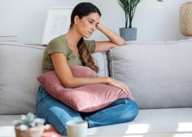 Nachdenkliche Frau auf Couch mit Kissen